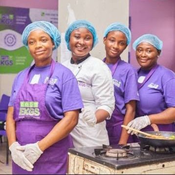 Four students in EKGS aprons smiling at the stove
