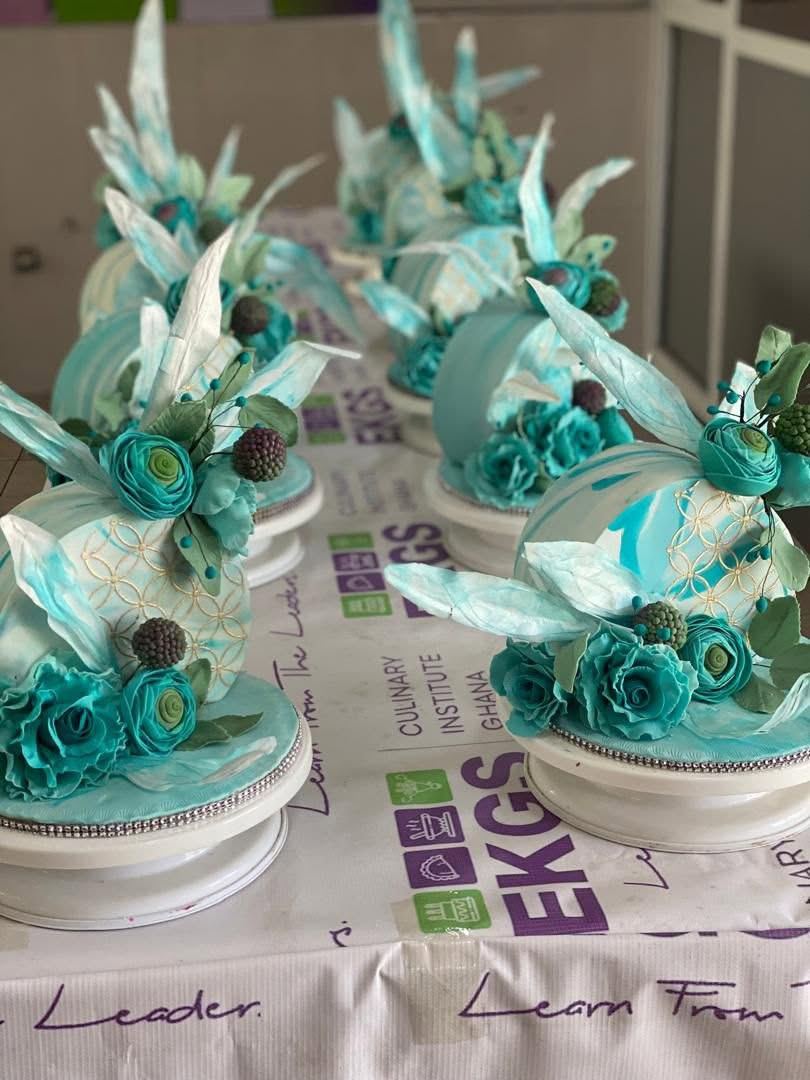 Row of student cakes with teal sugar roses and wafer paper sails